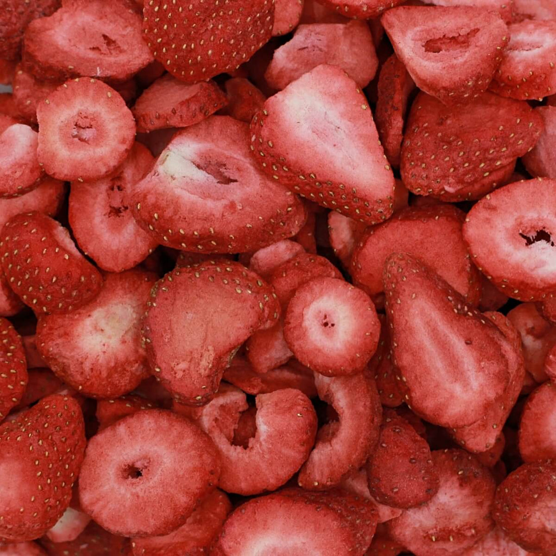Dried strawberries in a bowl on a wooden surface with fresh strawberries beside it.