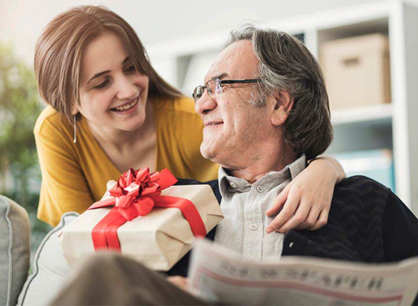The image shows a daughter presenting a gift to her father, a common moment associated with holidays such as Father's Day.