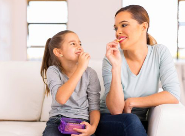 This image shows a mother and daughter sitting on a couch and enjoying snacks together.